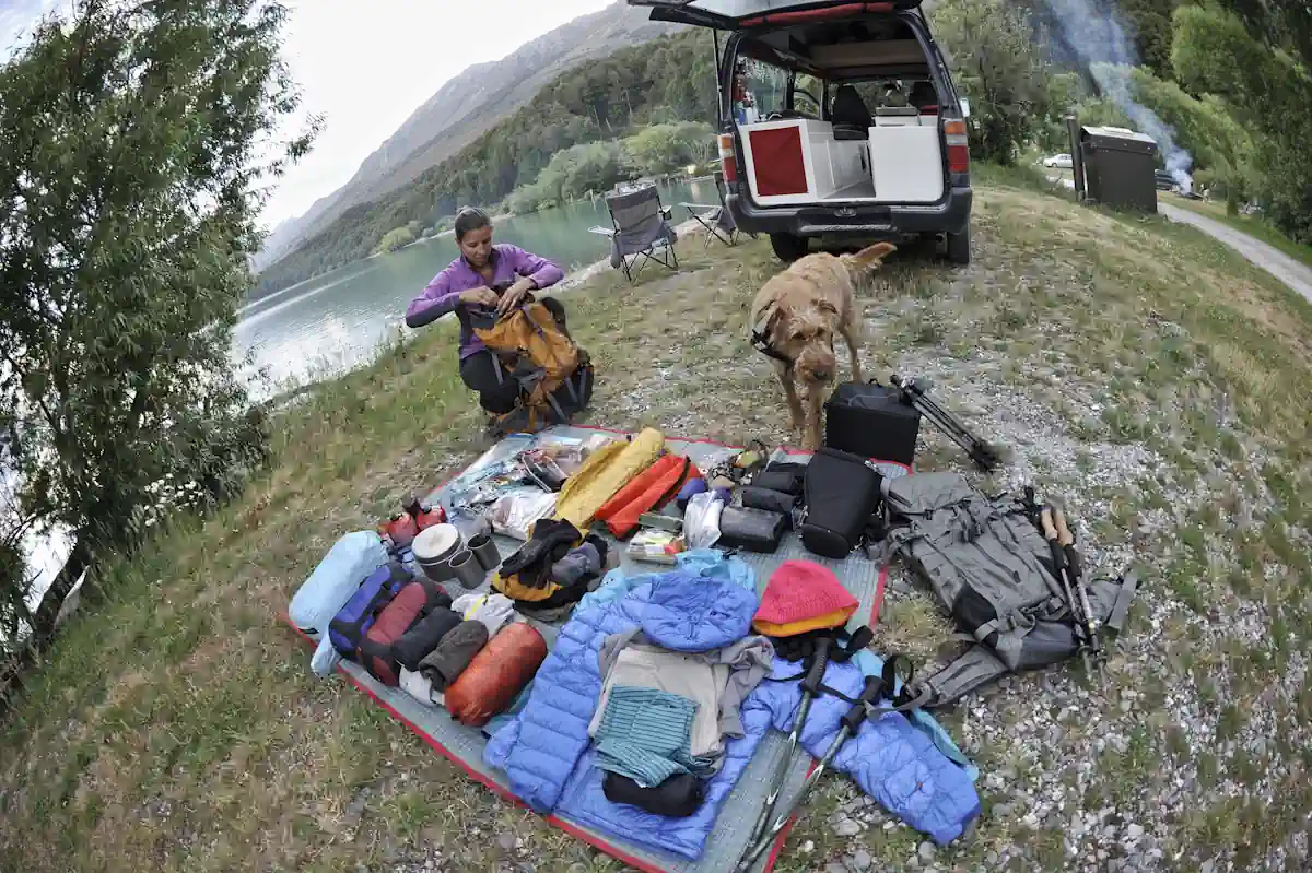 Une femme et un chien qui étale des équipements de raod trip sur le sol