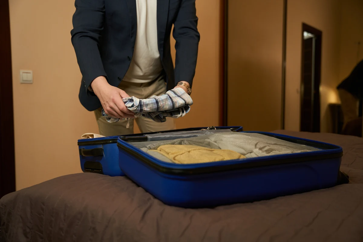 Un homme qui met des vêtements dans une valise posée sur le lit