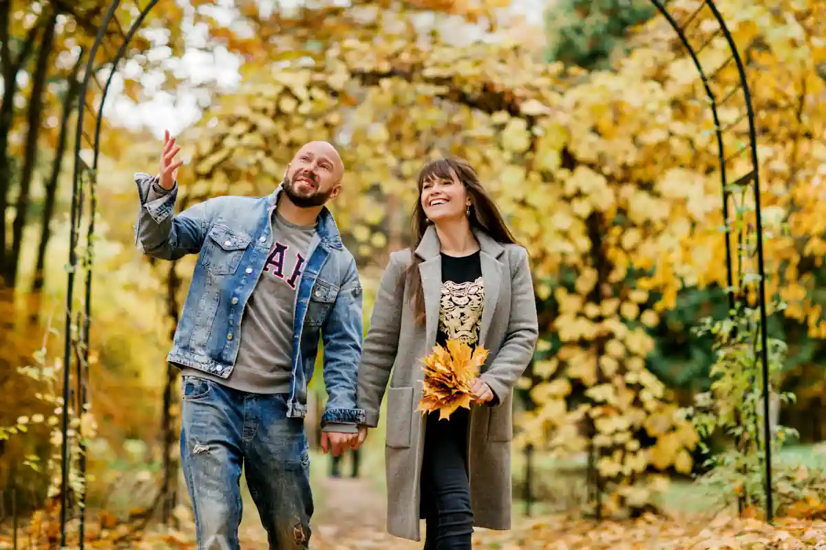 Un couple qui se balade au milieu des arbres avec des feuillages oranges