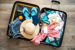Une valise ouverte sur le sol avec des tongs, un châpeau et des vêtements à l'intérieur