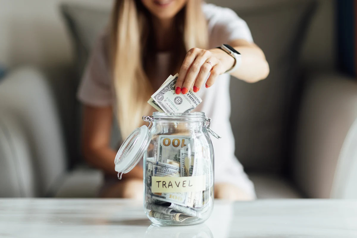 Une femme qui met de l'argent dans un bocal avec l'étiquette TRAVEL sur le devant