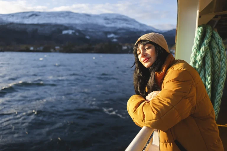 Une femme en blouson et avec un bonnet qui profite de la brise sur un bateau