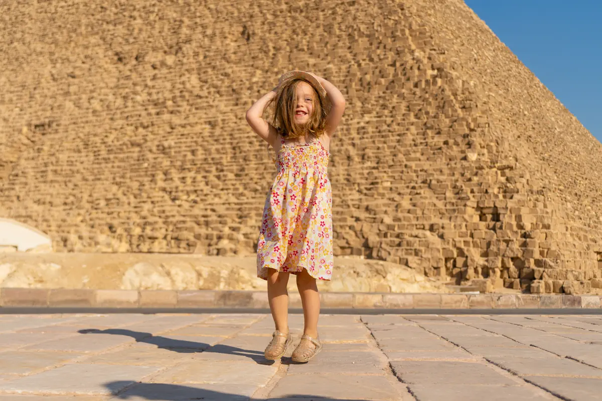 Une petite fille en robe et avec un chapeau devant une pyramide